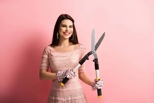Smiling, elegant girl in working gloves holding gardening scissors on pink background — Stock Photo