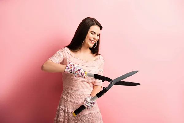 Happy girl in working gloves holding gardening scissors on pink background — Stock Photo