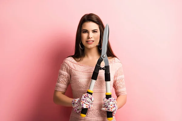 Elegant girl in working gloves holding gardening scissors on pink background — Stock Photo