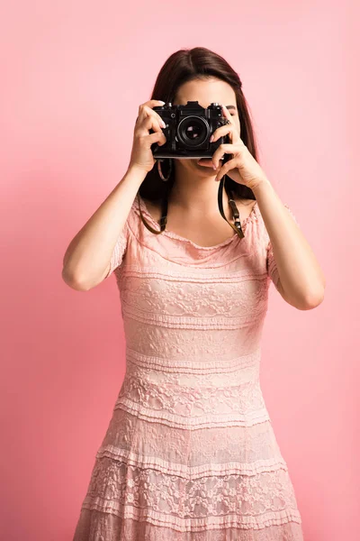 Fotógrafo en vestido elegante tomando fotos en cámara digital sobre fondo rosa - foto de stock