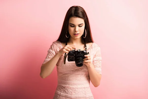 Pretty, attentive photographer looking at digital camera on pink background — Stock Photo