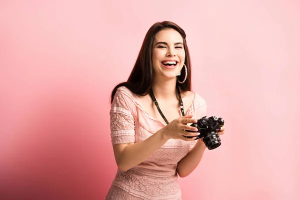 Щасливий фотограф сміється, тримаючи цифрову камеру на рожевому фоні — стокове фото