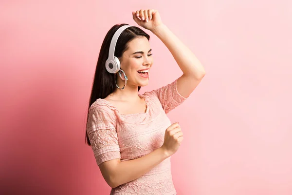 Menina feliz em fones de ouvido sem fio dançando e cantando em fundo rosa — Fotografia de Stock