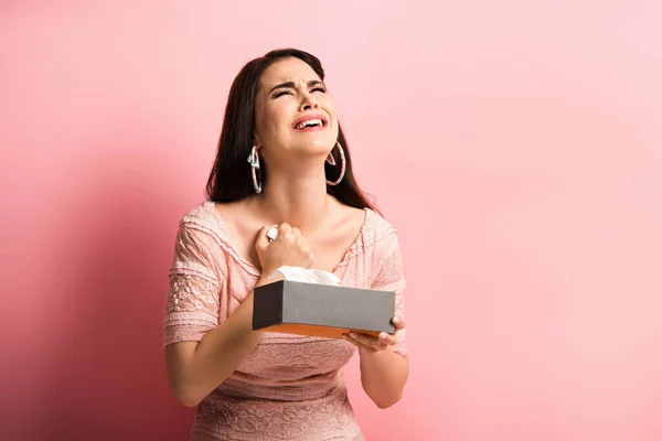 Chica molesta mirando hacia arriba y llorando mientras sostiene servilletas de papel sobre fondo rosa — Stock Photo