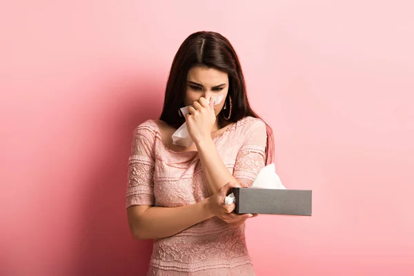 Menina doente esfregando nariz com guardanapo de papel no fundo rosa — Fotografia de Stock