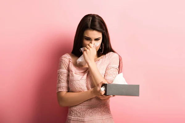 Niña enferma limpiando la nariz con servilleta de papel sobre fondo rosa - foto de stock