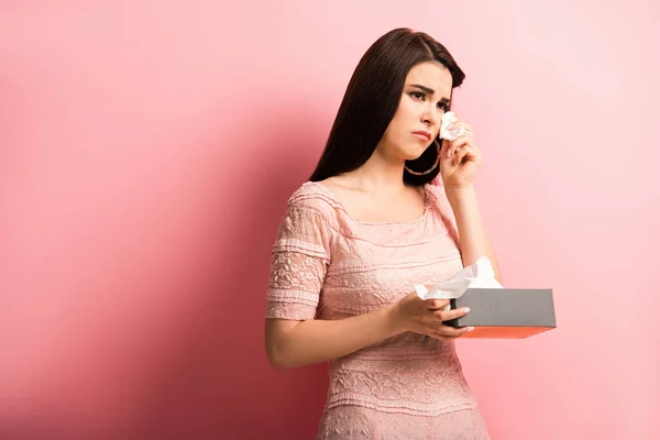 Offended girl crying and wiping tears with paper napkin on pink background — Stock Photo