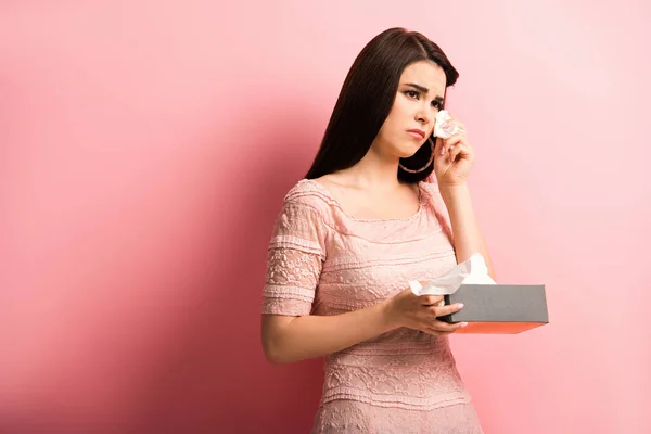 Chica ofendida llorando y limpiando lágrimas con servilleta de papel sobre fondo rosa - foto de stock