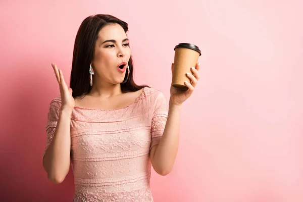 Изумленная девушка показывает вау жест, держа кофе, чтобы пойти на розовый фон — стоковое фото