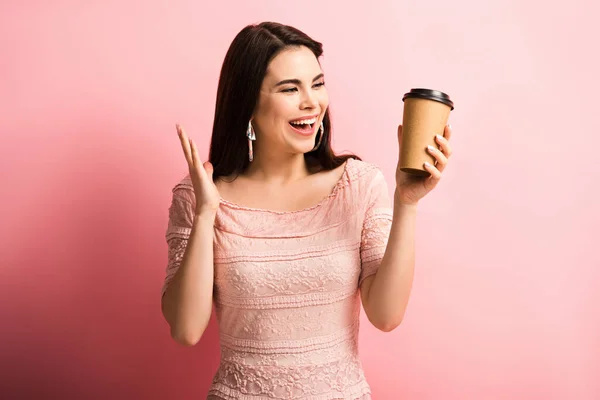 Glückliches Mädchen zeigt Wow-Geste beim Halten von Kaffee auf rosa Hintergrund gehen — Stockfoto