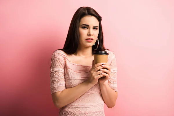 Offeso ragazza in possesso di caffè per andare mentre guardando la fotocamera su sfondo rosa — Foto stock