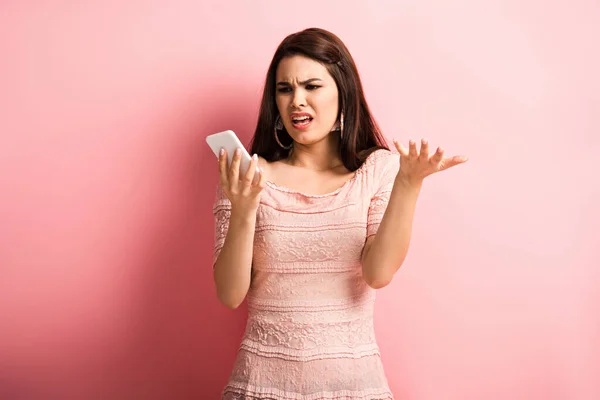 Menina descontente mostrando gesto de indignação durante vídeo chat no smartphone em fundo rosa — Fotografia de Stock