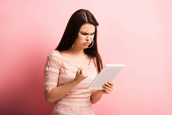 Сердита дівчина показує згорнутий кулак під час відеочату на цифровому планшеті на рожевому фоні — стокове фото