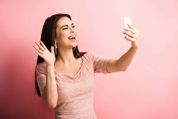 Щаслива дівчина махає рукою під час відео чату на смартфоні на рожевому фоні — стокове фото