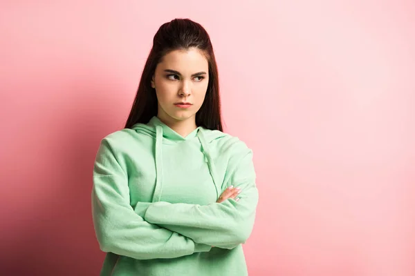 Offended girl looking away while standing with crossed arms on pink background — Stock Photo