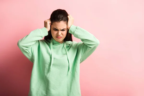 Agotada chica tocando la cabeza mientras sufre de dolor de cabeza sobre fondo rosa - foto de stock