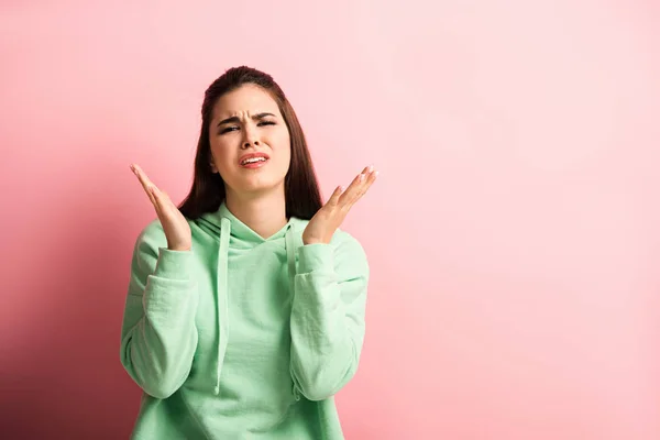 Upset girl looking at camera while standing with open arms on pink background — Stock Photo