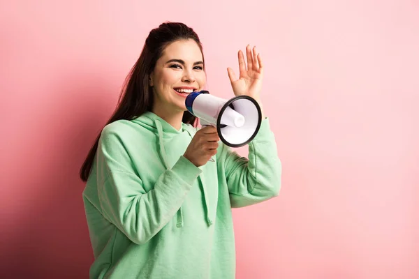 Heureuse fille agitant la main tout en parlant en mégaphone sur fond rose — Photo de stock