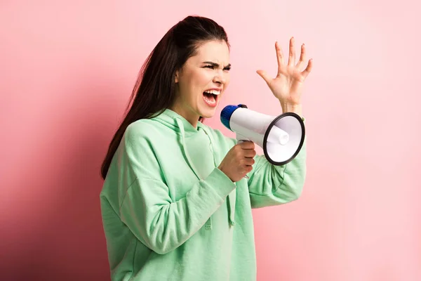 Сердита дівчина кричить в мегафоні, жестикулюючи з піднятою рукою на рожевому фоні — стокове фото