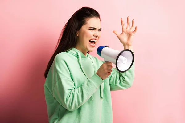 Fille en colère criant en mégaphone tout en faisant un geste avec la main levée sur fond rose — Photo de stock