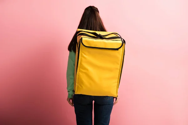 Back view of delivery woman carrying yellow thermo backpack on pink background — Stock Photo
