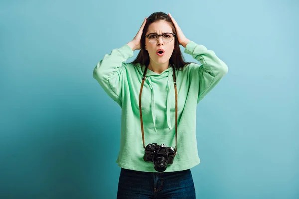 Schockierter Fotograf berührt Kopf beim Anblick der Kamera auf blauem Hintergrund — Stockfoto