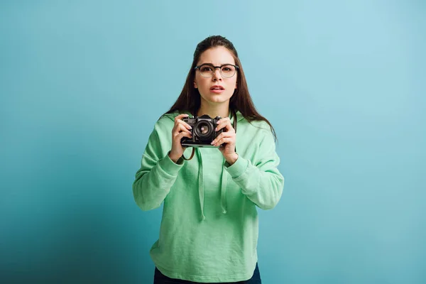Fotógrafo concentrado mirando a la cámara mientras sostiene la cámara digital sobre fondo azul - foto de stock