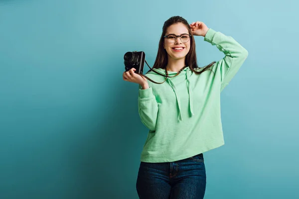 Fotógrafo feliz sosteniendo la cámara digital mientras sonríe sobre fondo azul - foto de stock