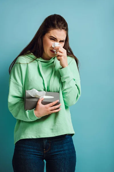 Malade fille essuyant nez avec serviette en papier sur fond bleu — Photo de stock