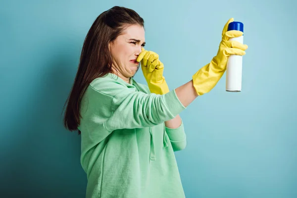 Displeased housewife plugging nose with hand while spraying air freshener on blue background — Stock Photo