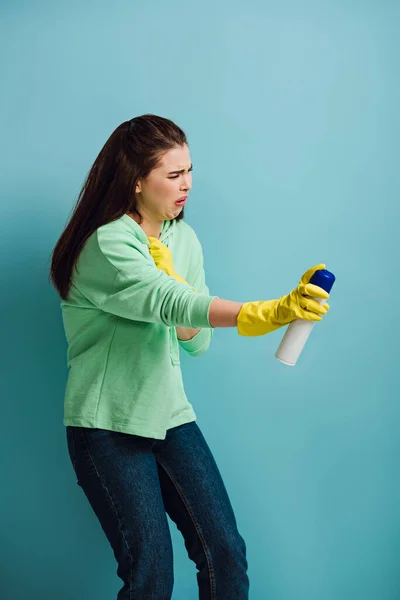 Недовольная домохозяйка гримасничает, распыляя освежитель воздуха на голубом фоне — стоковое фото