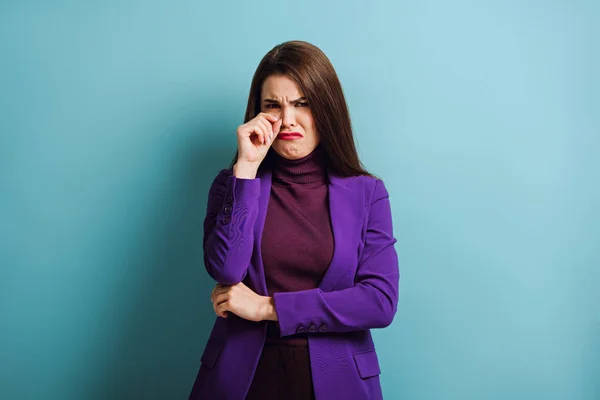 Offended girl crying and wiping tears with hand while standing on blue background — Stock Photo