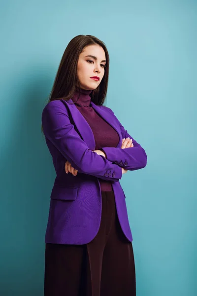 Upset girl looking down while standing with crossed arms on blue background — Stock Photo