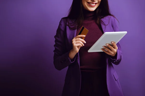 Corte vista de mulher sorridente segurando tablet digital e cartão de crédito em fundo roxo — Fotografia de Stock