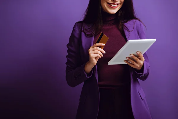 Vista recortada de la mujer sonriente sosteniendo tableta digital y tarjeta de crédito sobre fondo púrpura — Stock Photo