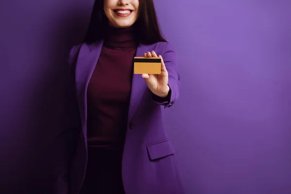 Обрезанный вид улыбающейся женщины, показывающей кредитную карту на фиолетовом фоне — стоковое фото