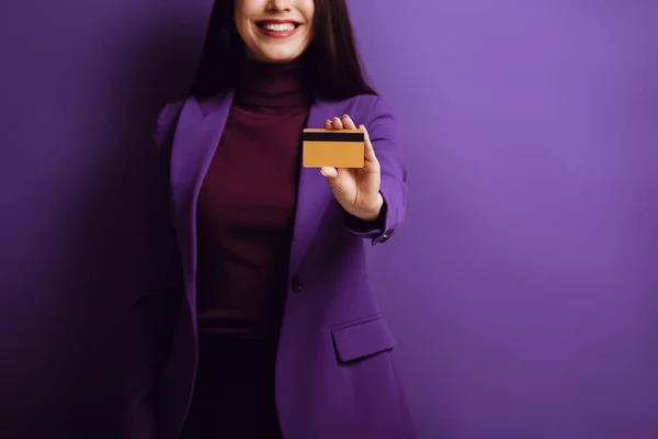 Cropped view of smiling woman showing credit card on purple background — Stock Photo