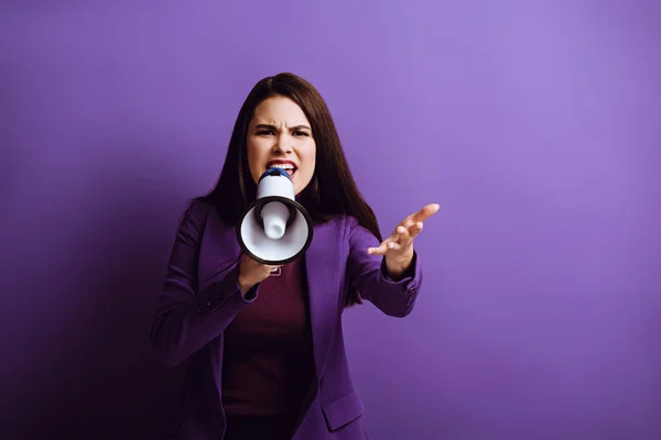 Irritée jeune femme criant en mégaphone tout en montrant un geste d'indignation sur fond violet — Photo de stock