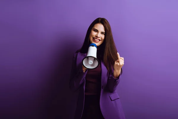 Fröhliche Frau zeigt Mittelfinger und hält Megafon auf lila Hintergrund — Stockfoto