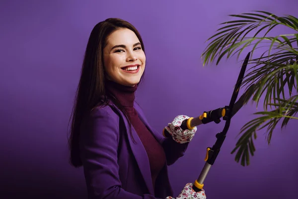 Souriant jeune femme usine de découpe avec ciseaux de jardinage sur fond violet — Photo de stock