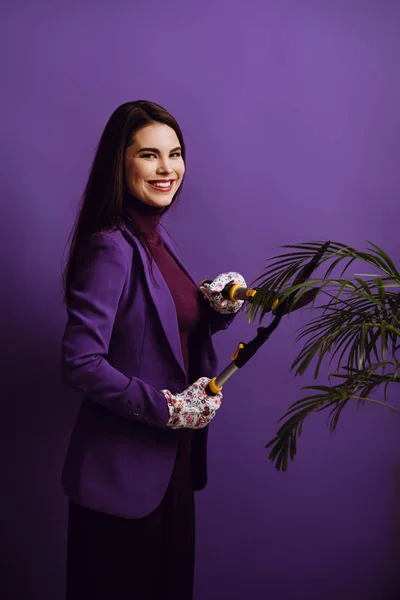 Feliz jovem mulher planta de corte com tesoura de jardinagem no fundo roxo — Fotografia de Stock