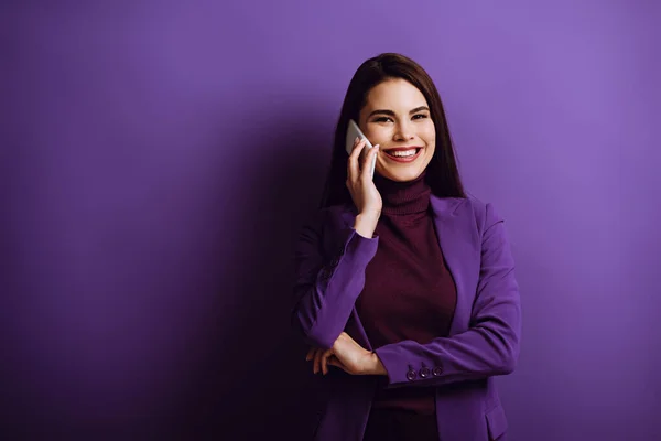 Positive junge Frau lächelt in die Kamera, während sie auf dem Smartphone auf lila Hintergrund spricht — Stockfoto