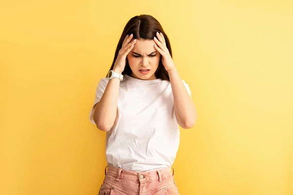 Müdes Mädchen berührt Kopf, während es an Kopfschmerzen leidet, isoliert auf gelb — Stockfoto