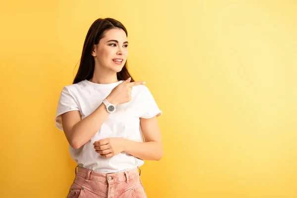 Sonriente chica mirando hacia otro lado y señalando con el dedo aislado en amarillo - foto de stock