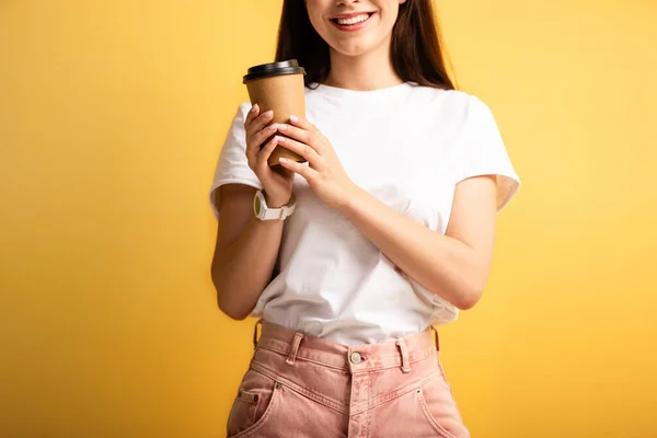 Cropped view of smiling girl holding coffee to go on yellow background — Stock Photo