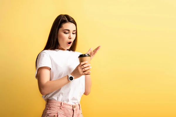 Überrascht Mädchen mit offenem Mund stehen, während Kaffee zu gehen isoliert auf gelb — Stockfoto