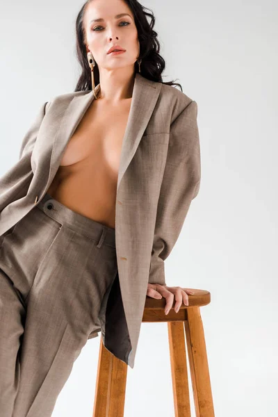 Stilvolle und sexy Frau im Anzug sitzt auf Hocker auf grauem Hintergrund — Stockfoto
