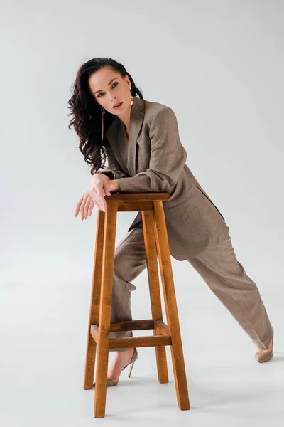 Stylish woman in suit on stool looking at camera on grey background — Stock Photo