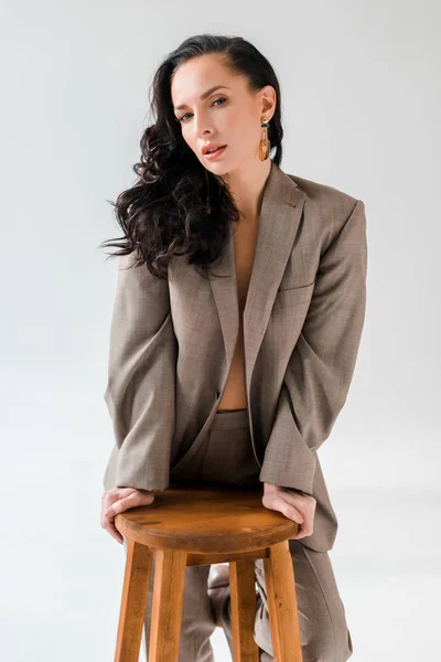 Stylische Frau im Anzug auf Hocker blickt in die Kamera auf grauem Hintergrund — Stockfoto