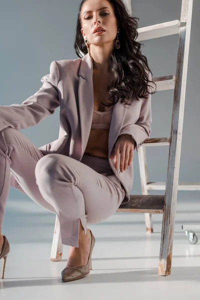 Sexy ed elegante donna in abito vicino scala guardando la fotocamera su sfondo grigio — Foto stock